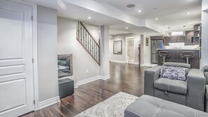 A spacious living area with a dark wood floor, a gray sofa set, a patterned rug, and a staircase leading to an upper level. - Charming basement retreat awaits you! (Markham)
