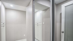 A hallway with a glass door leading to a room with a white door and a white cabinet. - Charming basement retreat awaits you! (Markham)