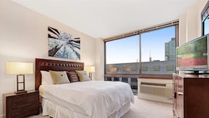 Ein Hotelzimmer mit einem großen Bett, einem Nachttisch, einem Fernseher und einem Fenster mit Blick auf die Stadt.