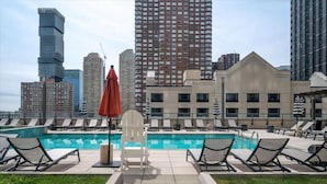 Une piscine sur le toit, dotée de chaises longues et offrant une vue sur les bâtiments de la ville.