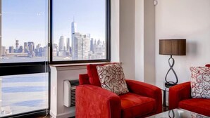 A modern living room with a large window offering a city skyline view. - Modern 2BR | Fully Equipped Kitchen | Near PATH by GLS (Jersey City)