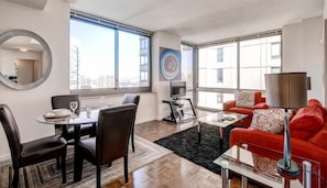 A modern living room with a dining area, large windows, a city view, a red sofa, and a TV.