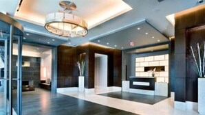 A spacious lobby with a modern design, featuring a central reception desk, a large chandelier, and a stone fireplace. - Modern 2BR | Fully Equipped Kitchen | Near PATH by GLS (Jersey City)