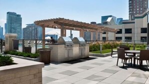 An outdoor patio area with a pergola, barbecue grill, and seating. - Modern 2BR | Fully Equipped Kitchen | Near PATH by GLS (Jersey City)