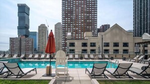 A rooftop pool with lounge chairs and a view of city buildings. - Spacious 2BR | Fully Equipped Gym | Near PATH by GLS (Jersey City)