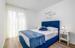 Camera da letto moderna con una testiera blu, biancheria da letto bianca e un comodino con una lampada.