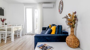 A modern living room with a dark blue sofa, a woven vase with dried flowers, and a dining area with a white table and chairs. - Beautiful apartment in Rovinj with WiFi (Rovinj)