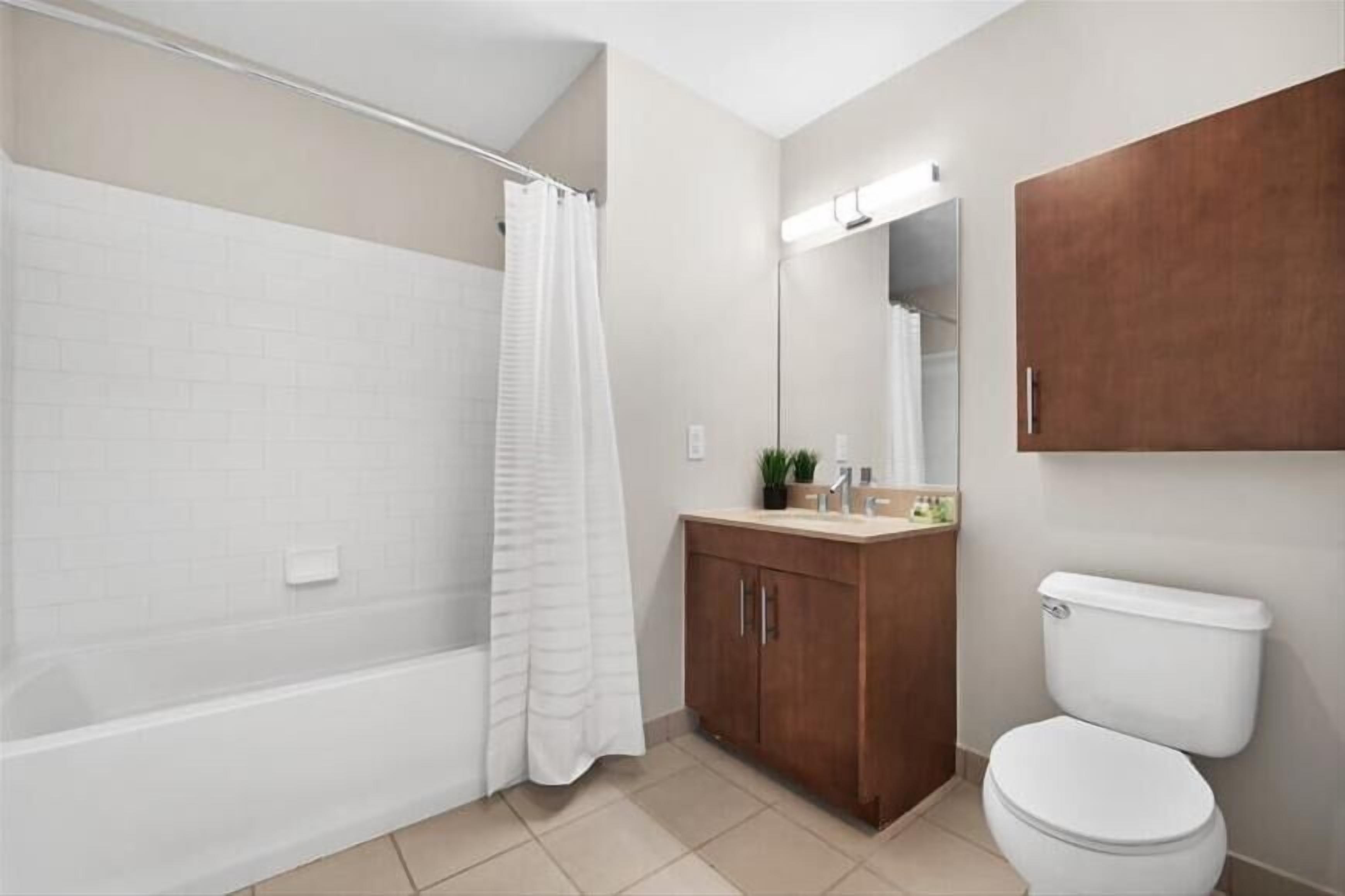 A bathroom with a bathtub, a toilet, a wooden cabinet, and a mirror.