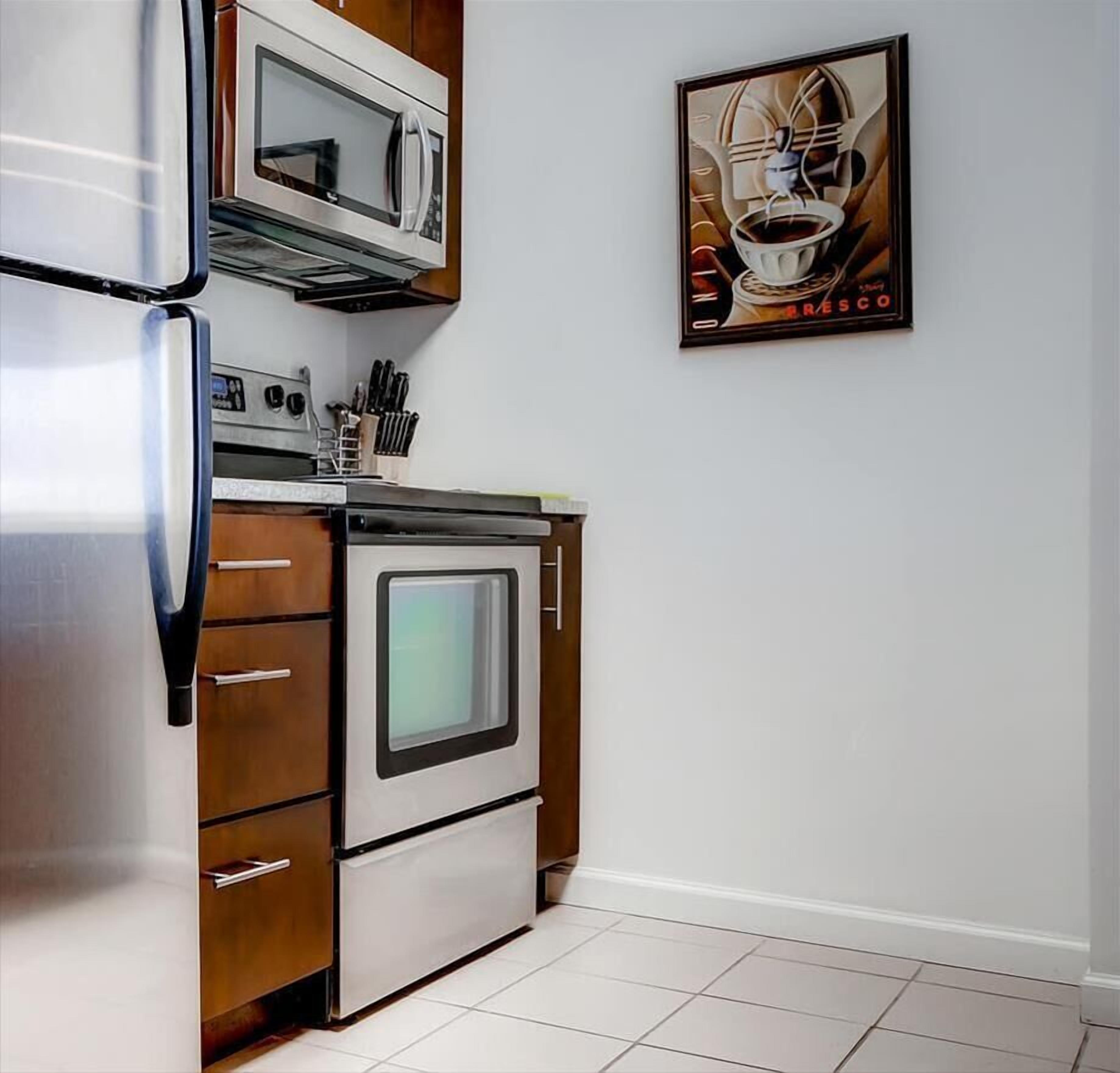 A kitchen with a stainless steel refrigerator, a microwave, and an oven. There is a knife block on the counter and a framed picture on the wall.