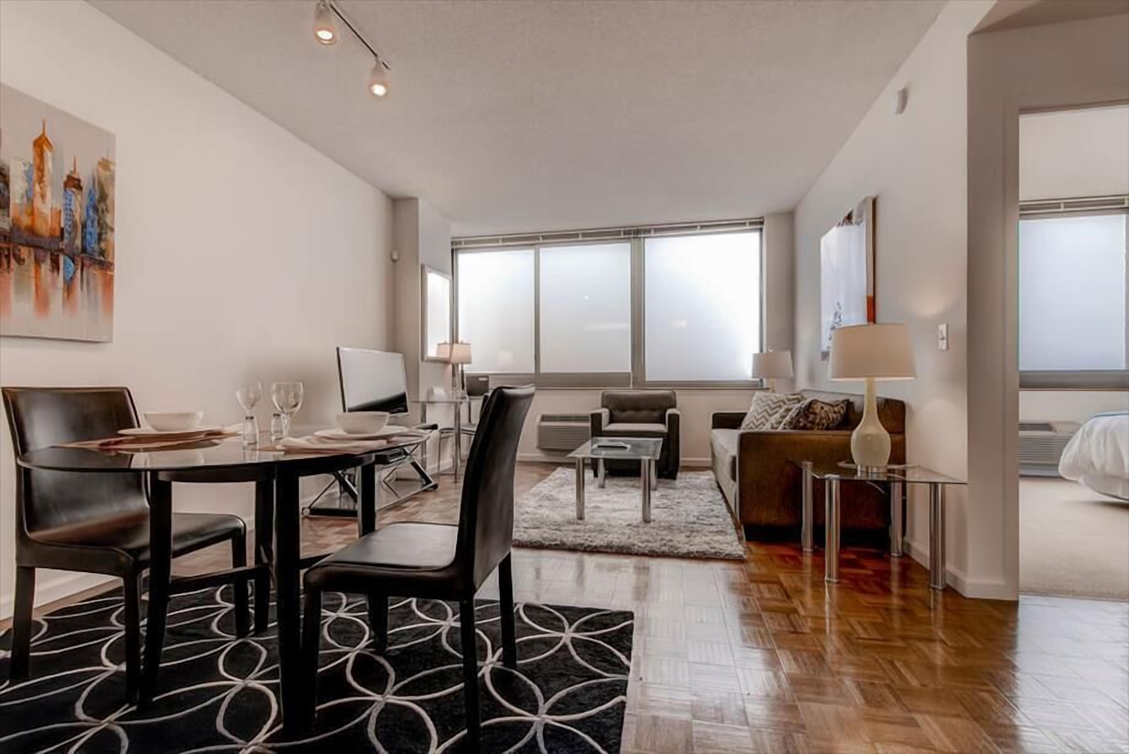 A modern living room with a dining area, large windows, and a cityscape painting on the wall.