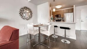 A modern kitchen with white cabinets, a stainless steel refrigerator, and a microwave. There is a dining area with a white table and chairs, and a red chair in the foreground.