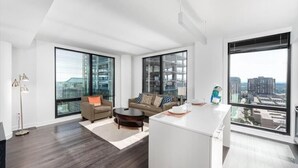 A modern living room with a large window, a sofa, a coffee table, and a kitchen area with a white countertop. - The Spectrum at RTC Nearby | High Speed Internet | Fairfax (Reston)