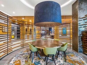 A modern conference room with a round table, green chairs, a large blue pendant light, and wooden slats on the walls.