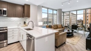 A modern kitchen with white cabinetry, stainless steel appliances, and a large window offering a city view.