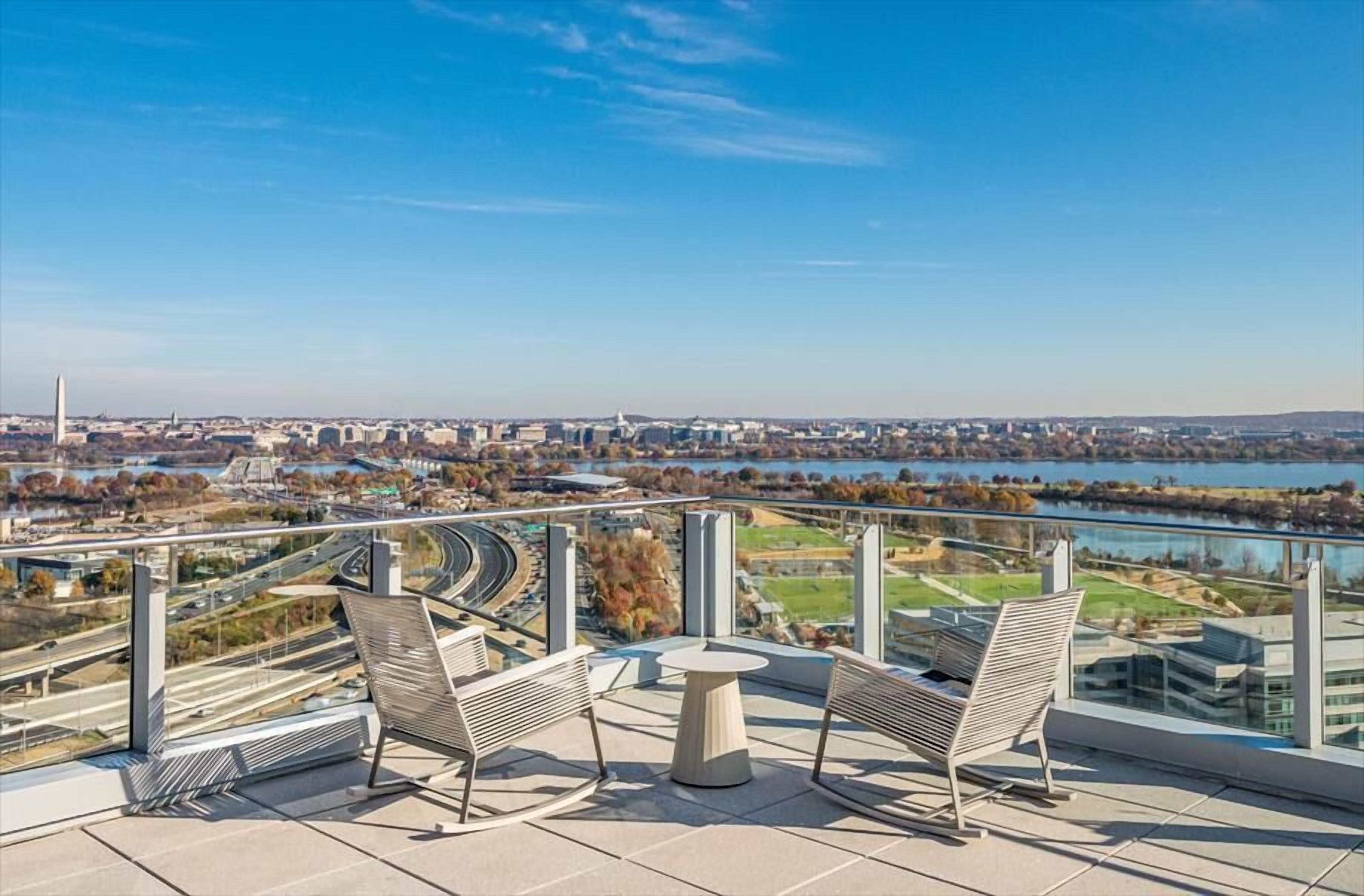 Ein Balkon mit zwei Stühlen und einem Tisch mit Blick auf eine Stadtlandschaft, in der ein Fluss, Autobahnen und ein weit entferntes Denkmal zu sehen sind.