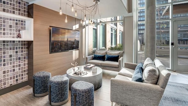 A modern living room with a cityscape painting, a sofa set, ottomans, and a coffee table. - Arlington Virginia 2BR | Crystal City | Easy DC Access | by GLS (Arlington)