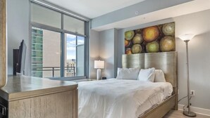 Ein modernes Hotelzimmer mit einem großen Bett, einem Schreibtisch, einem Bild an der Wand und Blick auf die Stadt durch das Fenster.