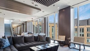 Ein modernes Wohnzimmer mit einer Eckcouch, einem Couchtisch und einem Sessel. Eine Treppe führt zu einer weiteren Ebene, und große Fenster bieten Blick auf die Stadt.
