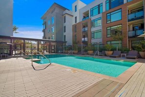 A modern hotel with a rooftop pool, outdoor seating, and a covered area with umbrellas.