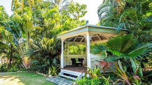 A gazebo with a wooden deck and a white lattice roof, surrounded by lush tropical vegetation. - Magnetic Island Resort Studio - Relax, sun, swim, fish, beach and lovely gardens (Nelly Bay)