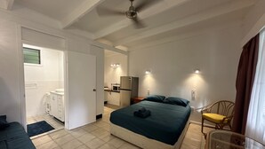 A bedroom with a bed, a chair, a small table, and a kitchenette in the background. - Magnetic Island Resort Studio - Relax, sun, swim, fish, beach and lovely gardens (Nelly Bay)
