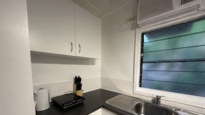 A modern kitchen with white cabinets, a black countertop, a stainless steel sink, and a window with textured glass. - Magnetic Island Resort Studio - Relax, sun, swim, fish, beach and lovely gardens (Nelly Bay)
