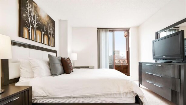 A modern hotel room with a large bed, a flat-screen TV, a dresser, and a painting on the wall. - Private & Clean 1BR | Work Remote | Hoboken Riverfront | Easy access to NYC (Hoboken)