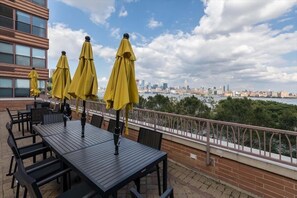 Un patio al aire libre con mesas y sillas, sombrillas amarillas y vista al horizonte de la ciudad.
