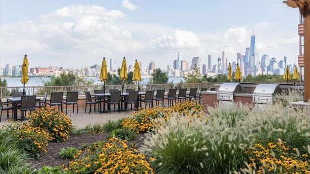 An outdoor seating area with yellow umbrellas, a grill, and a view of a city skyline.