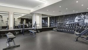 Une salle de sport moderne équipée de matériel de musculation, de miroirs et ornée d’une fresque murale sur le thème de la boxe.