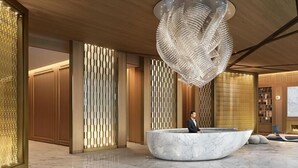 Un hall d’entrée moderne avec un comptoir de réception en marbre, des panneaux muraux aux motifs géométriques et une sculpture au plafond qui attire l’attention.