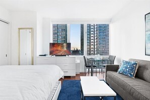 A modern hotel room with a large bed, a desk with a computer, a dining area, and a sofa.