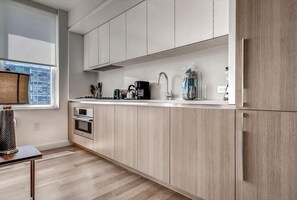 Una cocina moderna con gabinetes de madera clara, encimera blanca y electrodomésticos de acero inoxidable.