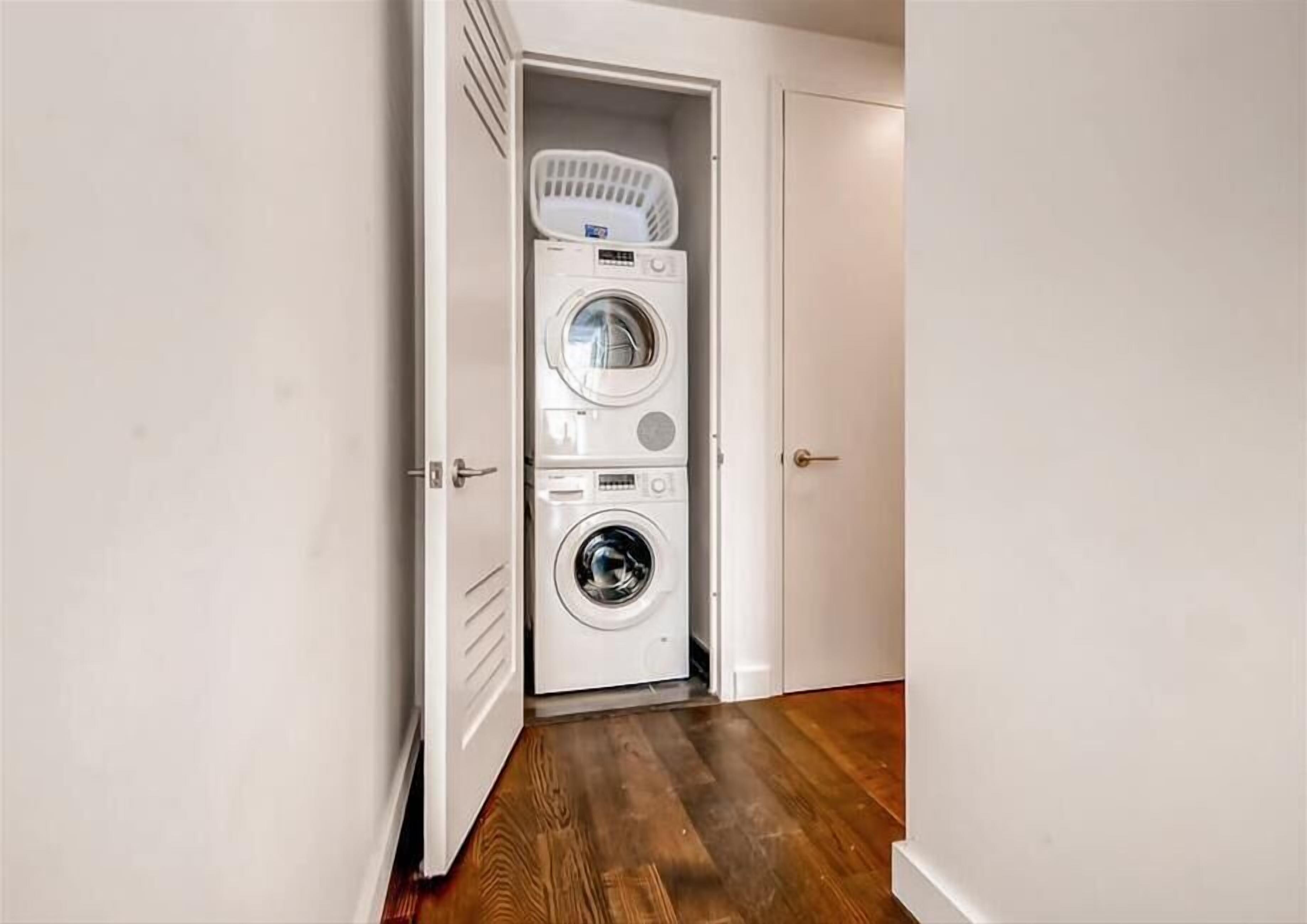 A laundry room with a stacked washer and dryer, a basket, and a wooden floor.
