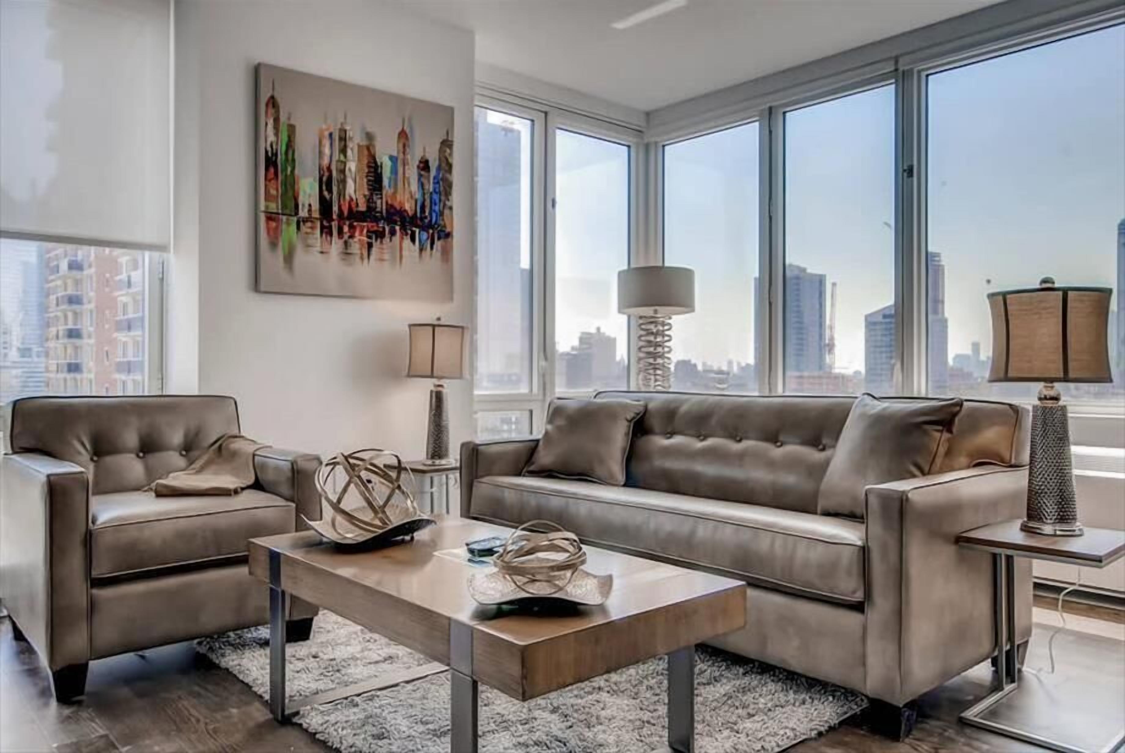 Un salon moderne avec un ensemble de canapés, une table basse et une vue sur la ville grâce à de grandes fenêtres.