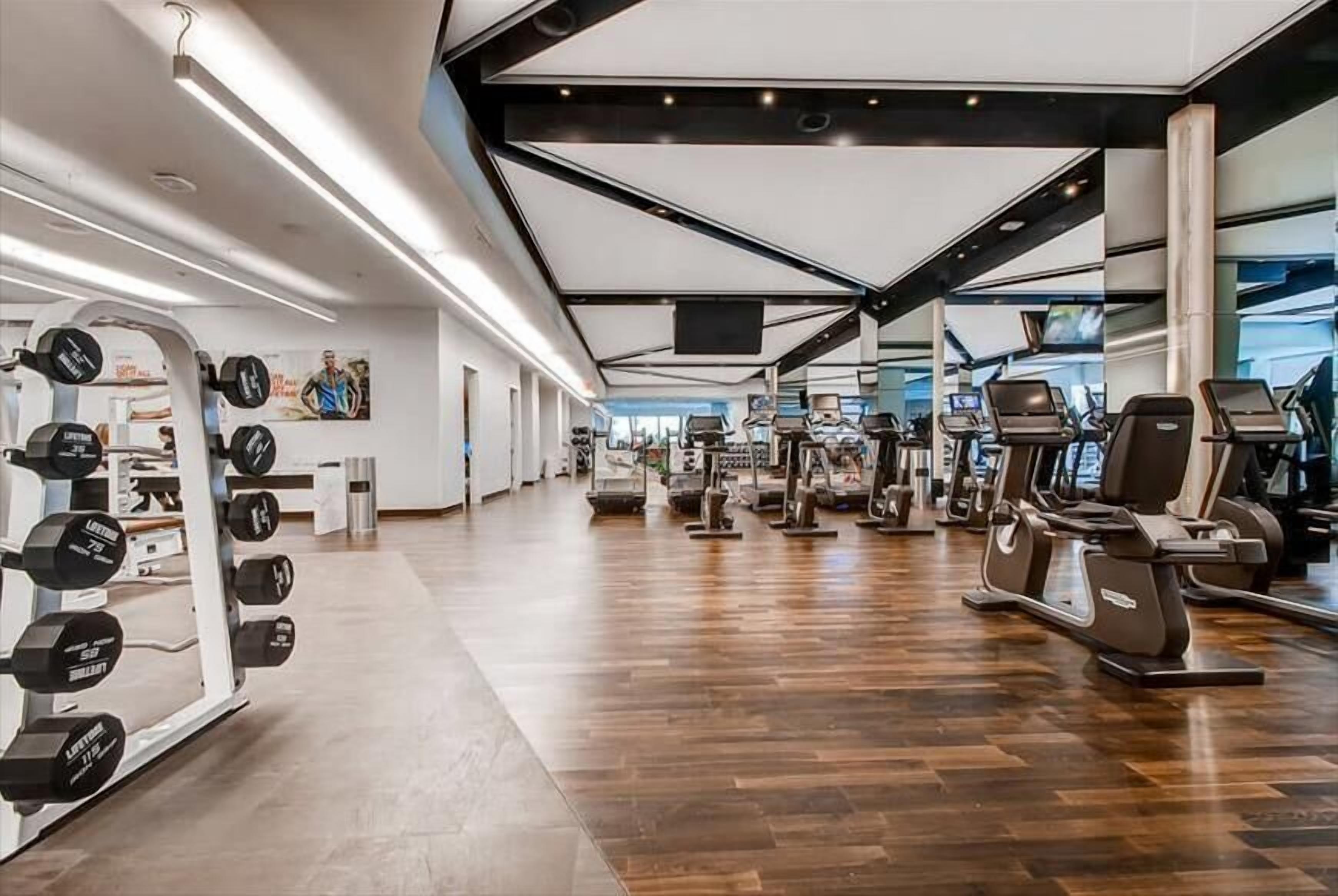 Un gimnasio moderno con diversos equipos de ejercicio, incluyendo cintas de correr y máquinas de pesas, y suelo de madera.