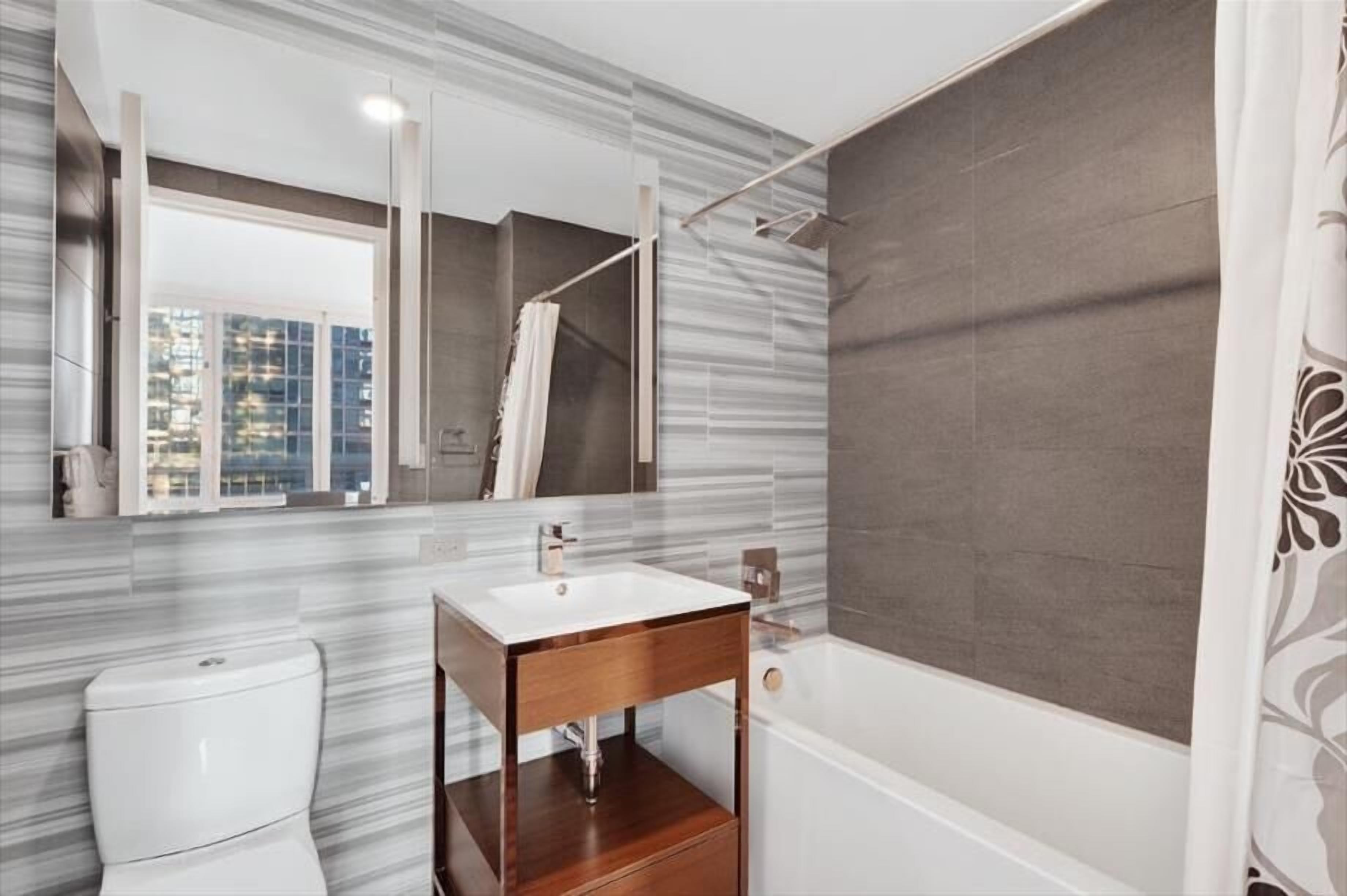 A modern bathroom with a white toilet, a wooden vanity with a sink, and a large mirror.