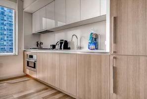 A modern kitchen with light wood cabinets, a stainless steel range, a built-in oven, and a window providing a view of the city.