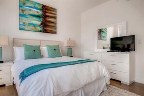 A modern bedroom with a large bed, a TV, and artwork on the walls.