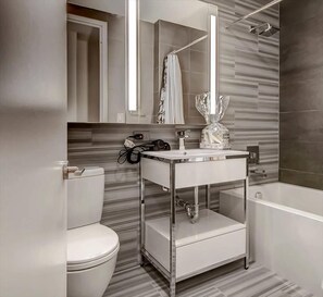 A modern bathroom with a toilet, a sink with a mirror, and a bathtub. - Private Fully Furnished 1BR | Washer & Dryer | Midtown West | by GLS (New York)