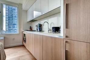 Cocina moderna con armarios de madera clara, un lavamanos de acero inoxidable y una ventana con vista a un paisaje urbano.