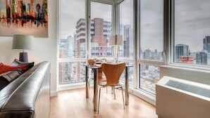 Un salon moderne avec une table en verre, un canapé en cuir et une vue sur la ville grâce à de grandes fenêtres.