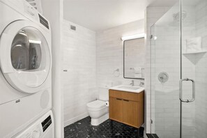 A compact bathroom with a washing machine, toilet, sink, and glass shower enclosure.