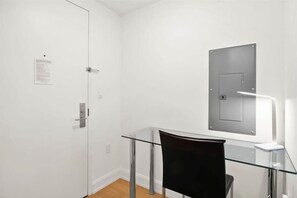 A room with a glass table, a black chair, a white door, and a wall-mounted light fixture.