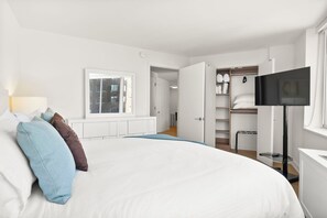 Ein Schlafzimmer mit Bett, Kissen, Fernseher, Kleiderschrank und Fenster.