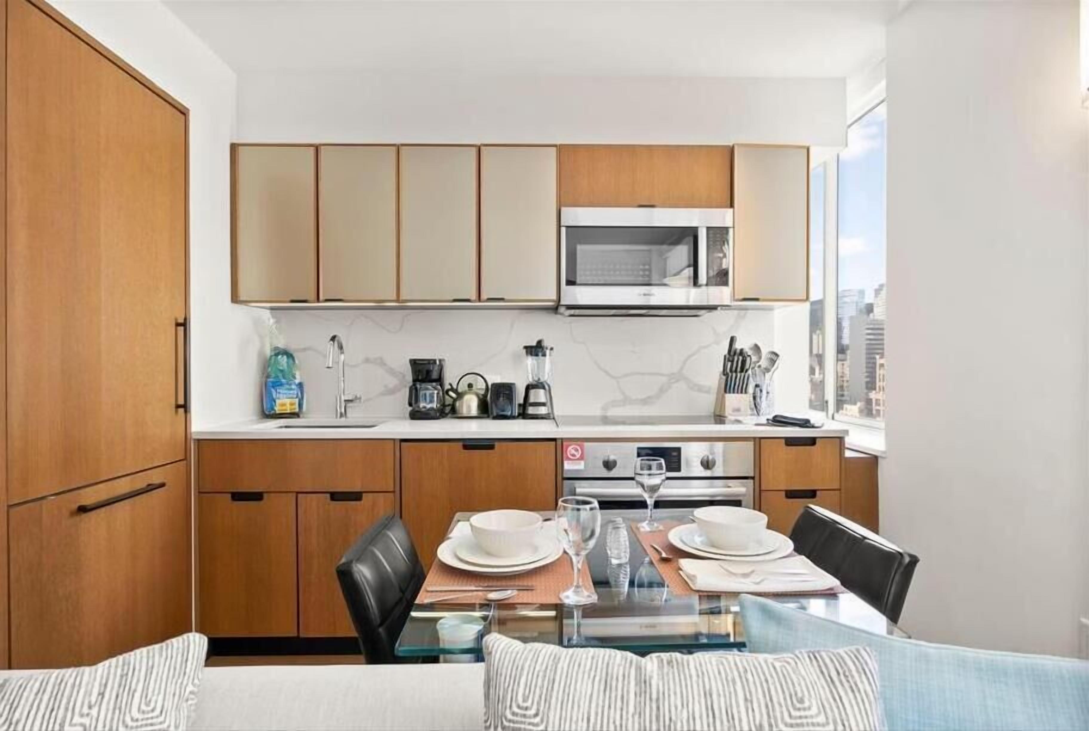 A modern kitchen with wooden cabinets, a microwave, and a dining area with a glass table and chairs.