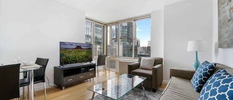 A modern living room with a glass coffee table, a sofa, a TV, and a dining area with chairs and a table.