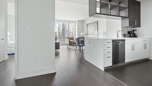 A modern kitchen with white cabinetry, a built-in dishwasher, and a large window overlooking a cityscape. - Upper West Side Apartments with Hudson River Views (New York)