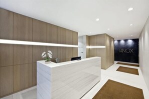 A modern reception area with a light-colored reception desk, wooden panel walls, and a black wall with the word "INOX".