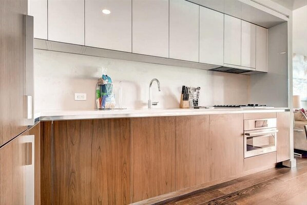 Una cocina moderna con armarios de madera, una encimera blanca, un extractor de acero inoxidable y un horno empotrado.